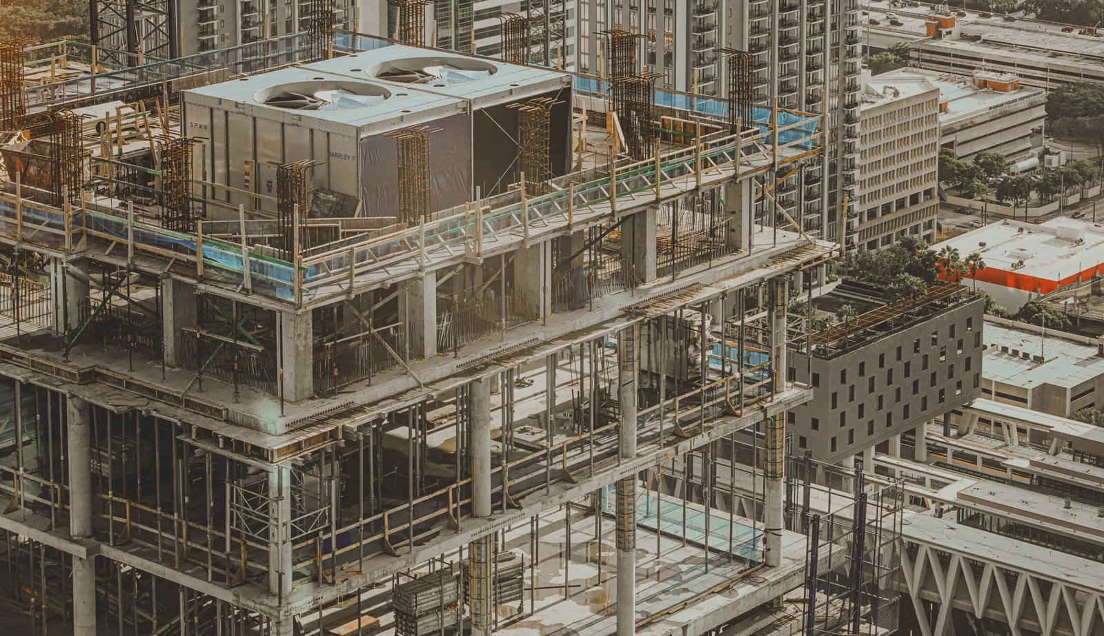 Construction site on a high-rise under development: exposed concrete floors, steel rebar, and scaffolding across multiple levels with a cityscape in the background | Beachy Construction